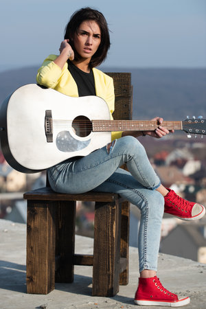 A young woman plays guitar. Creative musician play an acoustic guitar outdoors. Music guitar passion. Guitar performance. Artist expressing emotions through sound. Youth music culture.の写真素材
