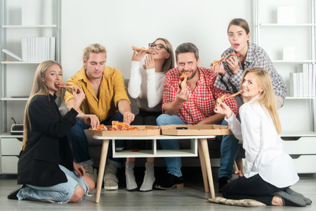 Group of friends eating pizza. Pizza with friends. Friends enjoying delicious pizza in a living room. Happy friends share pizza.の写真素材