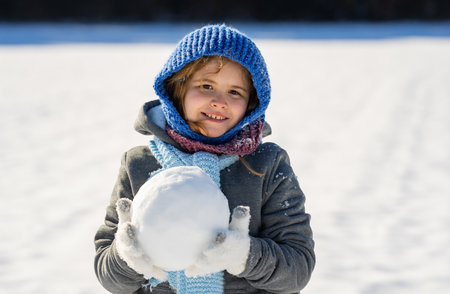 Child with rosy cheeks outdoors in winter. Cozy winter. Smiling child winter portrait close-up. Happy child outdoors in cold weather. Child in warm clothes in snow outdoor portrait.の写真素材