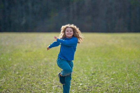 Child running on field. Happy kid running outdoors. Child jumping and running in nature. Kid running in a meadow. Summer fun for active child. Playful kid freedom. Carefree childhood in nature.の写真素材