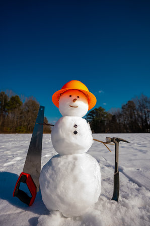 Snowman builder with construction equipment tools in snow. Snow man worker hold saw and hammer. Winter construction concept. Winter construction site greeting card. Snowman construction worker.の写真素材