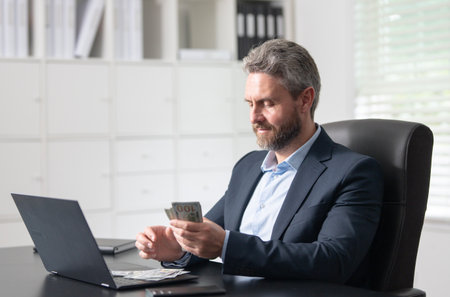 Business success concept. Businessman counts money at his office desk. Business man freelancer counts dollars in a corporate workspace. A handsome entrepreneur count money.の写真素材