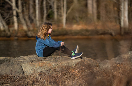 Kid on a pier near the river. Kid walk on rocks by the river. Child thoughtful outdoors. Casual teenager on nature. Calm and quiet time near the river. Peaceful childhood.の写真素材