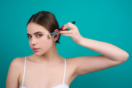 Woman applies powder on the face using makeup brush. Girl doing contouring apply blush on cheeks....