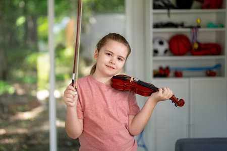 Kid playing violin at home. Child practicing classical violin indoors. Young violinist learning music in cozy interior. Kid playing acoustic violin during music lesson. Child practicing violin skill at home.の写真素材