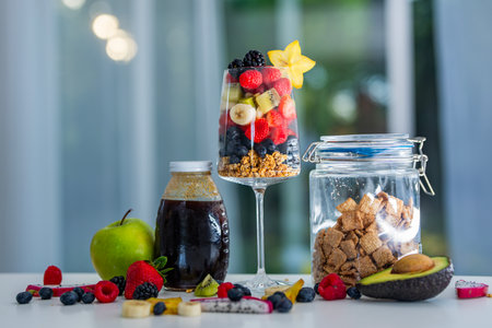 Fruit salad with granola, berries, banana, kiwi, and tropical fruits in glass.の写真素材