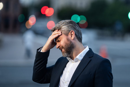 Tired business man outdoors suffering from a headache. Man relieving pain from a migraine. Financial problems and stress. Business crisis and bankruptcy concept. Business man worried and stressed.の写真素材