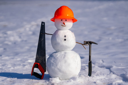 Cute snow man builder. Snowman engineer holds hammer and saw.の写真素材