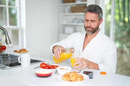 Hispanic Man eats breakfast in the kitchen. Guy enjoys fresh food at the kitchen table in the morning. A man eats cereal and fruit in the kitchen. Man eating healthy food in the kitchen.の写真素材