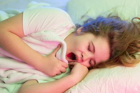 Child yawning after sleep. Kid yawning in the morning. Child yawning under soft blanket. Kid yawning in cozy bed.の写真素材