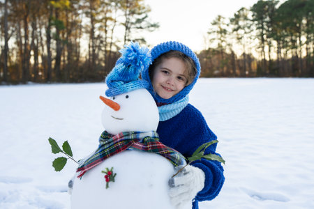 Child playing with snowman in snow field. Kids winter activity. Kids winter creativity in snowy field. Kid building snowman. Kids winter fun.の写真素材