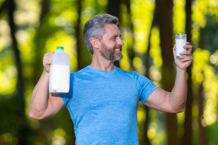 A healthy man holds a glass of fresh milk outdoors after a workout. Organic milk for energy and...