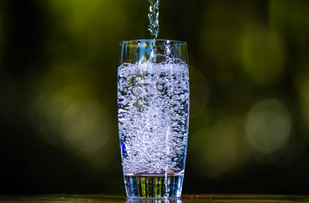Glass and water pouring on the green background. Water pouring into glass on wooden table outdoors....