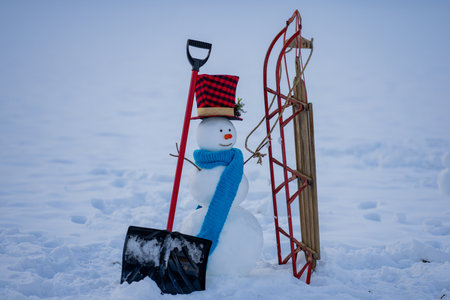 Creative winter card with snow man. Snowman ready to remove snow. Cute snowman prepared for snow removal. Snowman in winter landscape with snow shovel.の写真素材