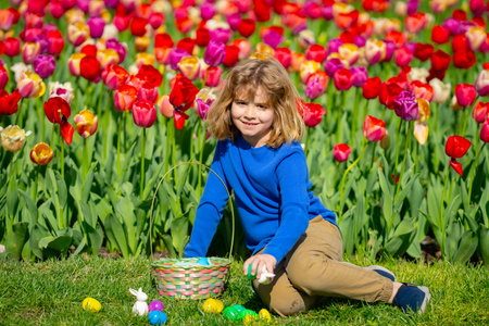 Child on Easter egg hunt among blooming tulips. Happy kid holding colorful Easter eggs in spring...