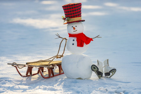 Snowman and sled in snow. Cute snow man portrait. Happy snowman shining. Snowman in winter light. Holiday winter setting.の写真素材