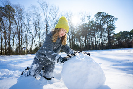 Happy winter. Child in warm winter clothes play with snow. Kid rolling snowball on winter morning....