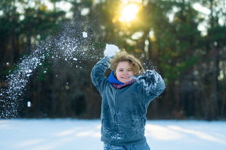 Laughing child in snow battle. Child throwing snow chunk. Kid playing snow games. Active winter child portrait. Excited child playing in snow. Kid enjoying winter fun. Winter kid play snowball.の写真素材