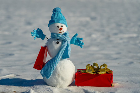 Snowman with Christmas gifts in a winter holiday sale scene. Snowman offering a holiday gift. Winter shopping fun. Snowman with holiday surprise. Snowman with shopping bags. Winter gifting concept.の写真素材