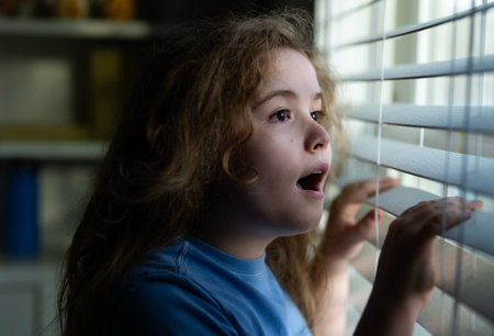 Kid waiting at home. Surprised child waiting at home near window. Surprised kid waiting and looking window out. Kid wait in a indoor moment. Child waiting on surprise by the window.の写真素材