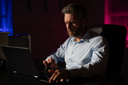 Business man using laptop late at night office. Overworked businessman at a desk with a hard office work. Business man on office night background. Worker bored and tired in dark office.の写真素材