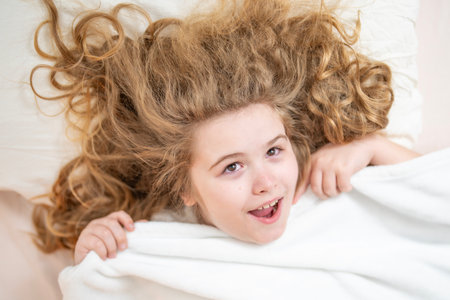 Portrait of kid waking up and stretching in comfortable bed. Kid waking up at home. Child waking up stretching arms in bedroom. Child waking in cozy bed.の写真素材