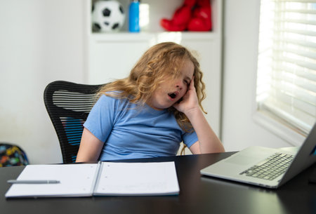 Sleepy bored kid at the school desk. Sleepy student needing a break from study. Sleepy id yawning while sitting at the laptop. Sleepy child study fatigue bored. Tired kid during bored learning.の写真素材