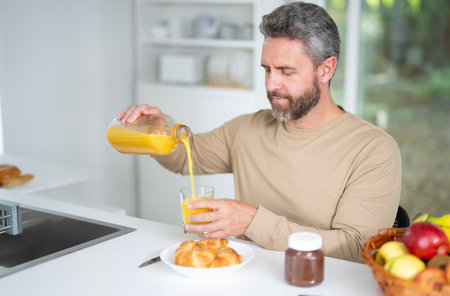 Man eats breakfast in the kitchen on a morning. A man enjoys fresh food at the kitchen table. A man eats cereal and fruit in the kitchen. Guy enjoys eggs and vegetables at the modern kitchen.の写真素材