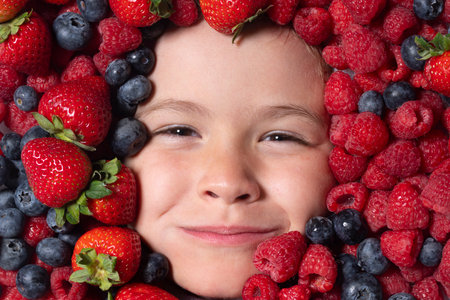 Vitamins from berrie. Child face with berries mix of strawberry, blueberry, raspberry, blackberry.の写真素材