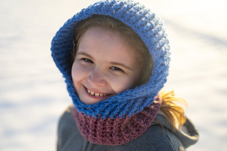 Child face on frosty day. Happy winter child portrait. Kid in knitted hood in winter. Cute kid in snow. Child winter lifestyle portrait. Winter holiday. Positive emotional child portrait in snow.の写真素材