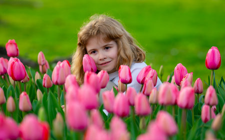 Tender Spring. Child play outdoors in a beautiful spring garden. Kid face in tulip flowers. Adorable little kid in blooming tulips garden on beautiful spring day. Happy child during spring blossom.の写真素材