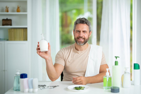 Beauty male model applying facial cream during a morning skincare routine at home. Beauty man using a moisturizing mask for anti-aging and rejuvenation. Male cosmetic facial treatment.の写真素材