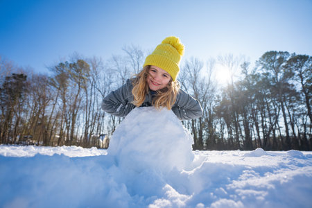 Happy winter. Child in warm winter clothes play with snow. Kid rolling snowball on winter morning. Cheerful kid playing with snow. Child building snowball outdoors. Cute girl enjoying winter weather.の写真素材