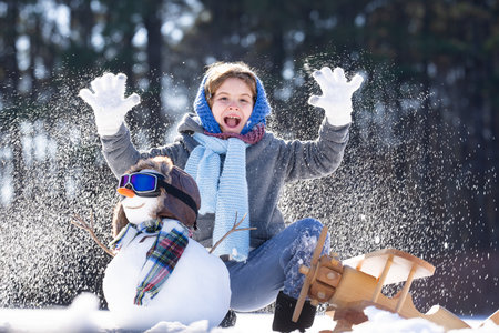 Child building a snowman on a winter day. Cute child building snowman outdoors. Child creating...