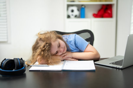 Sleepy bored kid at the school desk. Sleepy student needing a break from school. Sleepy id yawning while sitting at the laptop. Sleepy child study fatigue bored. Tired kid during bored learning.の写真素材