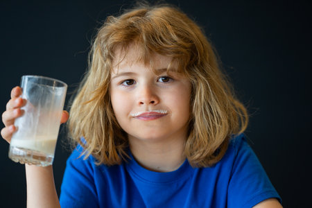 Cute kid with milk mustache portrait. Child with milk beverage at kitchen. Smiling boy with milk mustache kids face close-up. Child drinking glass of milk at home.の写真素材