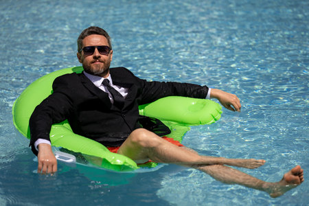 Eastern businessman taking a break. Tropical career escape. Stylish millennial enjoying success. Online work in pool. Wealthy tourist relaxing. Hot summer holiday retreat. Motivated freelancer.の写真素材