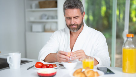 Hispanic Man eats breakfast in the kitchen. Guy enjoys fresh food at the kitchen table in the morning. A man eats cereal and fruit in the kitchen. Man eating healthy food in the kitchen.の写真素材