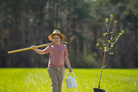Child plant tree in spring field. Little gardener with watering can and shovel. Child cultivating tree in garden.の写真素材