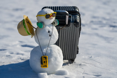 Snowman with luggage ready for holiday trip. Winter vacation starts with snowman. Funny snowman holding travel bag outdoors. Festive snowman tourist on winter adventure. New Year journey.の写真素材