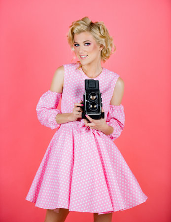 Pinup style photograph. Vintage photography theme. Blonde pinup girl with classic camera. Surprised blonde woman with retro camera. Creative feminine photoshoot in studio.の写真素材