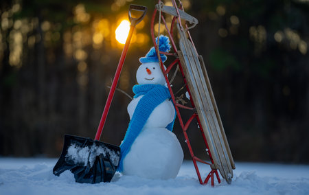Winter landscape with snowman, sled and snow shovel. Winter vibes snowman decoration with shovel and sled. Winter background with snowman for New Year greeting card. Cozy winter design with snowman.の写真素材