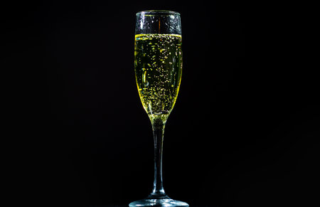 Champagne sparkling in a crystal glass. Pouring bubbly champagne with festive bubbles. Close-up of sparkling wine splash in elegant wineglass. Champagne drink with golden fizz on black background.の写真素材