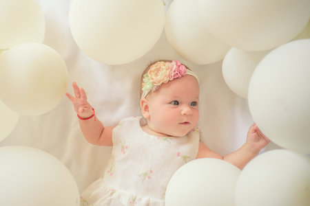 Smiling baby girl in dress lying on balloons. Cute infant portrait. Happy baby with balloons....