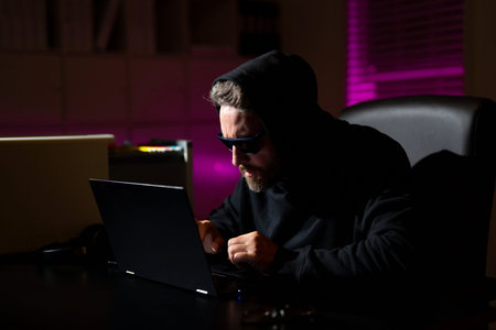 Hacker types on a laptop in a night office during a cyber attack. Hacker and stolen financial data...