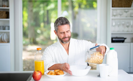 Man eats breakfast in the kitchen on morning. Man enjoys a healthy meal at the kitchen table. A man...
