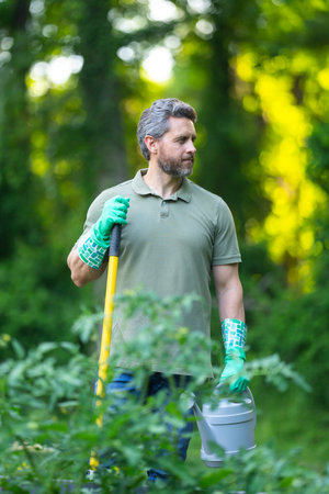 The gardener holds a watering can. Fresh plants need the gardener. A man gardens in the backyard. He...