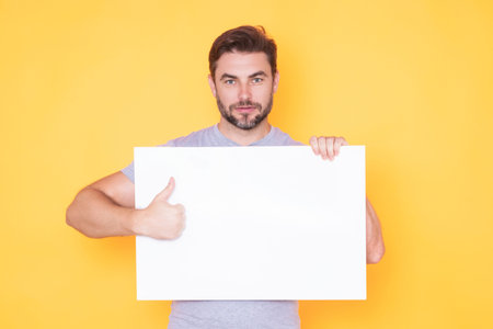 Man holding empty board on studio background. Male model with thumb up showing blank signboard with copyspace. Idea and offer. Your advertisement. Good choice, recommend like concept with copy space.の写真素材