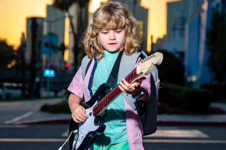 Cute boy plays on the electric guitar with funny face. Child with blonde curly hair playing guitar...