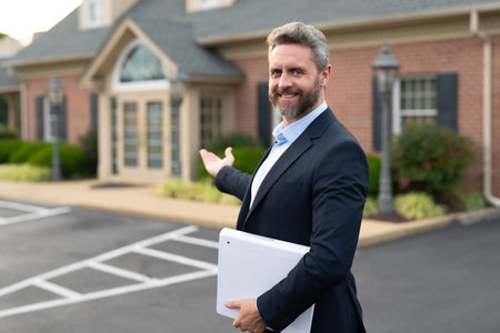 Real estate agent poses confidently in front of building ready for sale. Real estate entrepreneur closing deal. Mortgage agent buying a house. Realtor shows apartment. Business man near building.